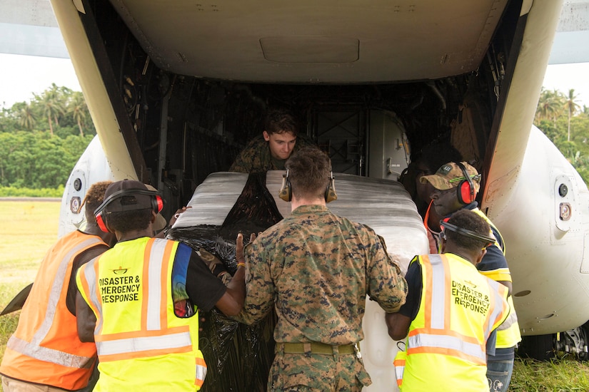 Marines load boxes of supplies into the open doorway of a parked aircraft.