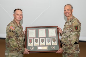 U.S. Army Maj. Gen. John V. Meyer III, the 1st Infantry Division and Fort Riley commanding general, gives a plaque to Command Sgt. Maj. Christopher L. Mullinax, the 1st Inf. Div. and Fort Riley command sergeant major, at Victory Hall on Fort Riley, Kansas, August 8, 2023. The plaque given contained a detailed history of the Big Red One patch dating back to 1918. (U.S. Army photo by Spc. Joshua Holladay)