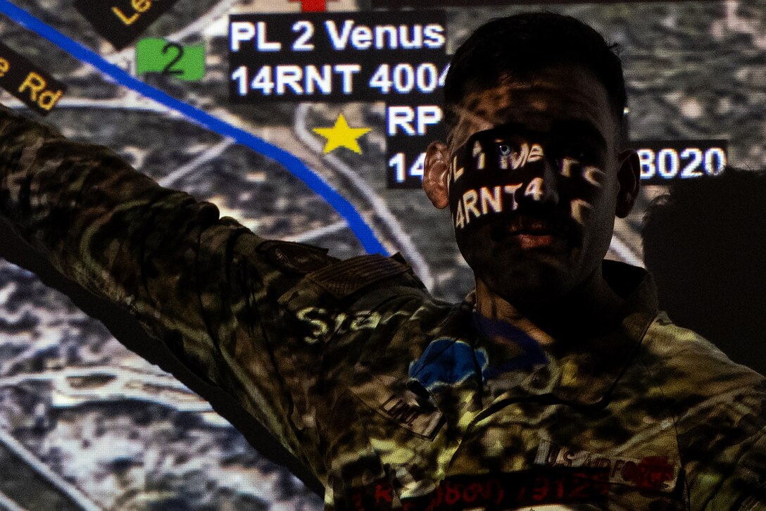 An airman stands before a projected image of a map which is reflected on their face.