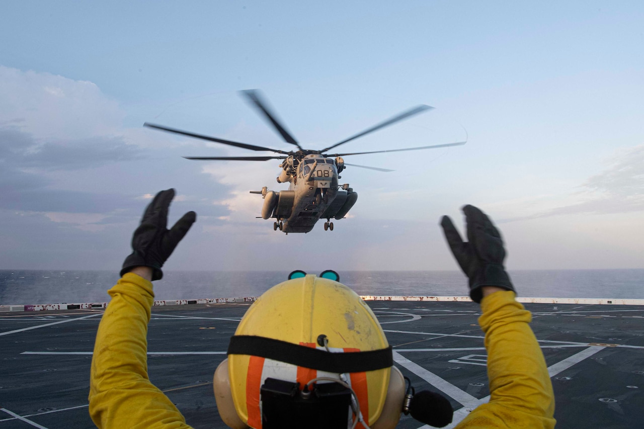 A sailor signals toward a helicopter from the deck of a ship.