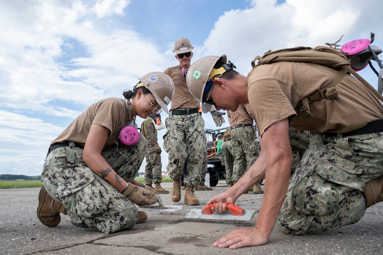 Sailors use tools to level out concrete.
