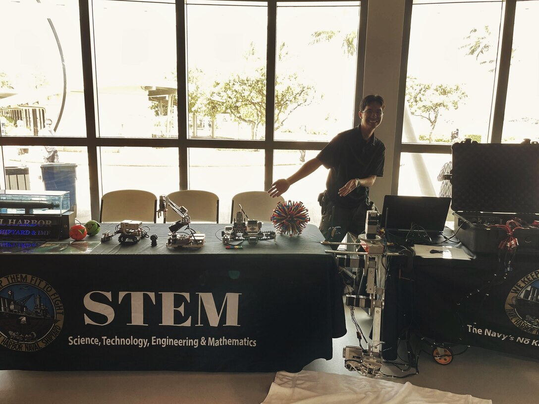 Pearl Harbor Naval Shipyard (PHNSY) Engineer Ryan Saito, from Code 100TO.32 Technology Insertion, gestures to the PHNSY booths that are set up and ready for students to interact with the hands-on demonstrations during a science, technology, engineering, and mathematics (STEM) event at the Pacific Fleet Submarine Museum.