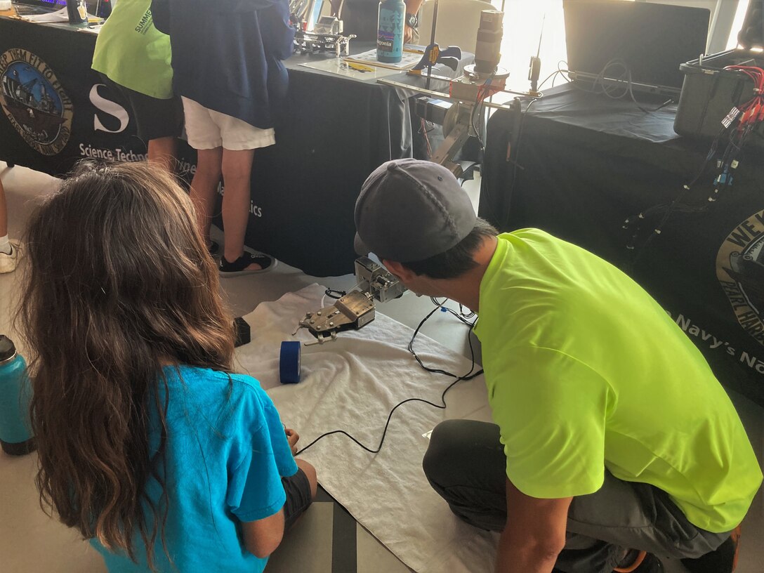 Pearl Harbor Naval Shipyard Engineer Vance Hashimoto, right, from Code 100TO.32 Technology Insertion, demonstrates how to use a robotic arm to students during a STEM event at the Pacific Fleet Submarine Museum