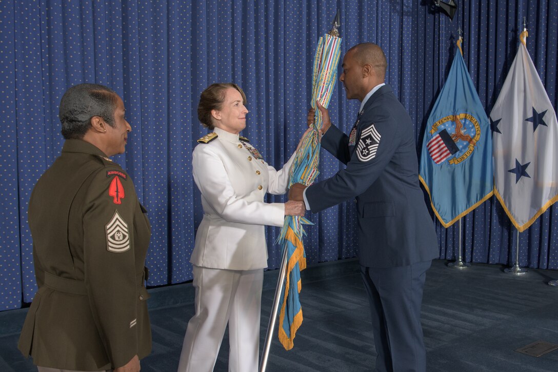A Navy officer hands a flag over to an Air Force noncommissioned officer.