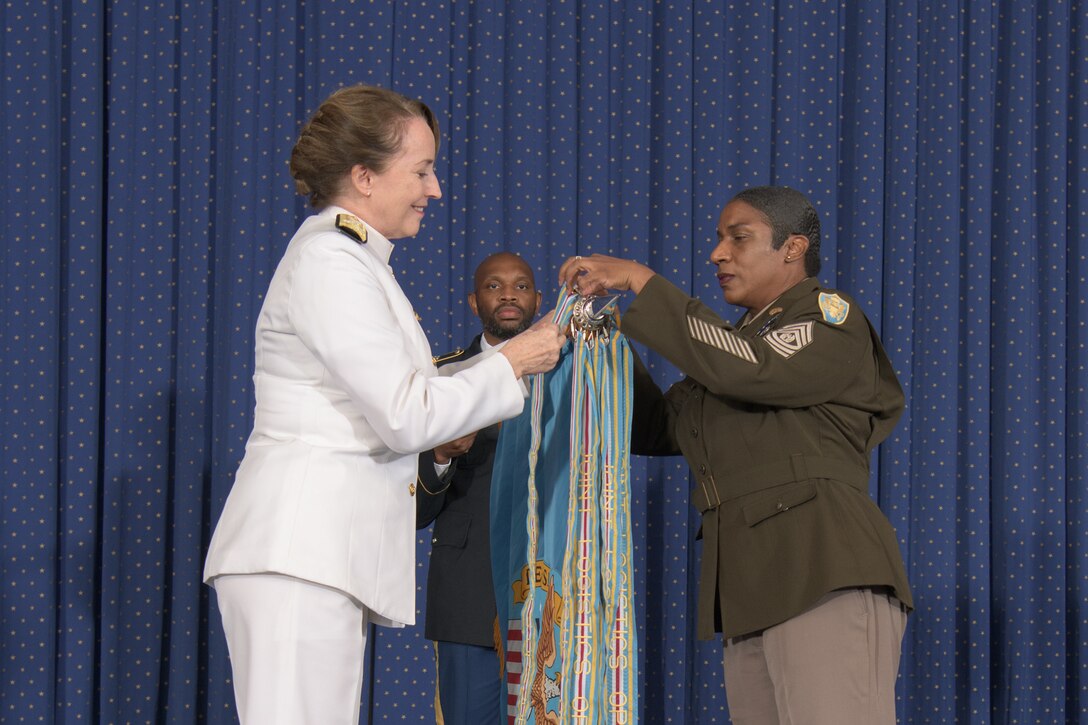 Two female military officers place a streamer on a flag.