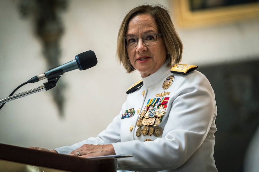 A woman in uniform speaks from a lectern displaying the U.S. Naval Academy crest.