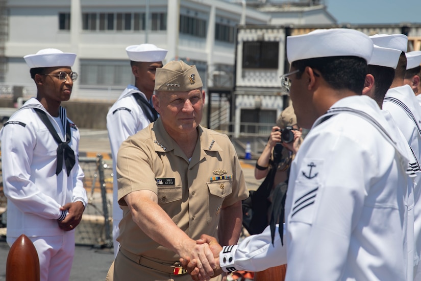 A man in uniform shakes hands with another man in uniform while boarding a ship.