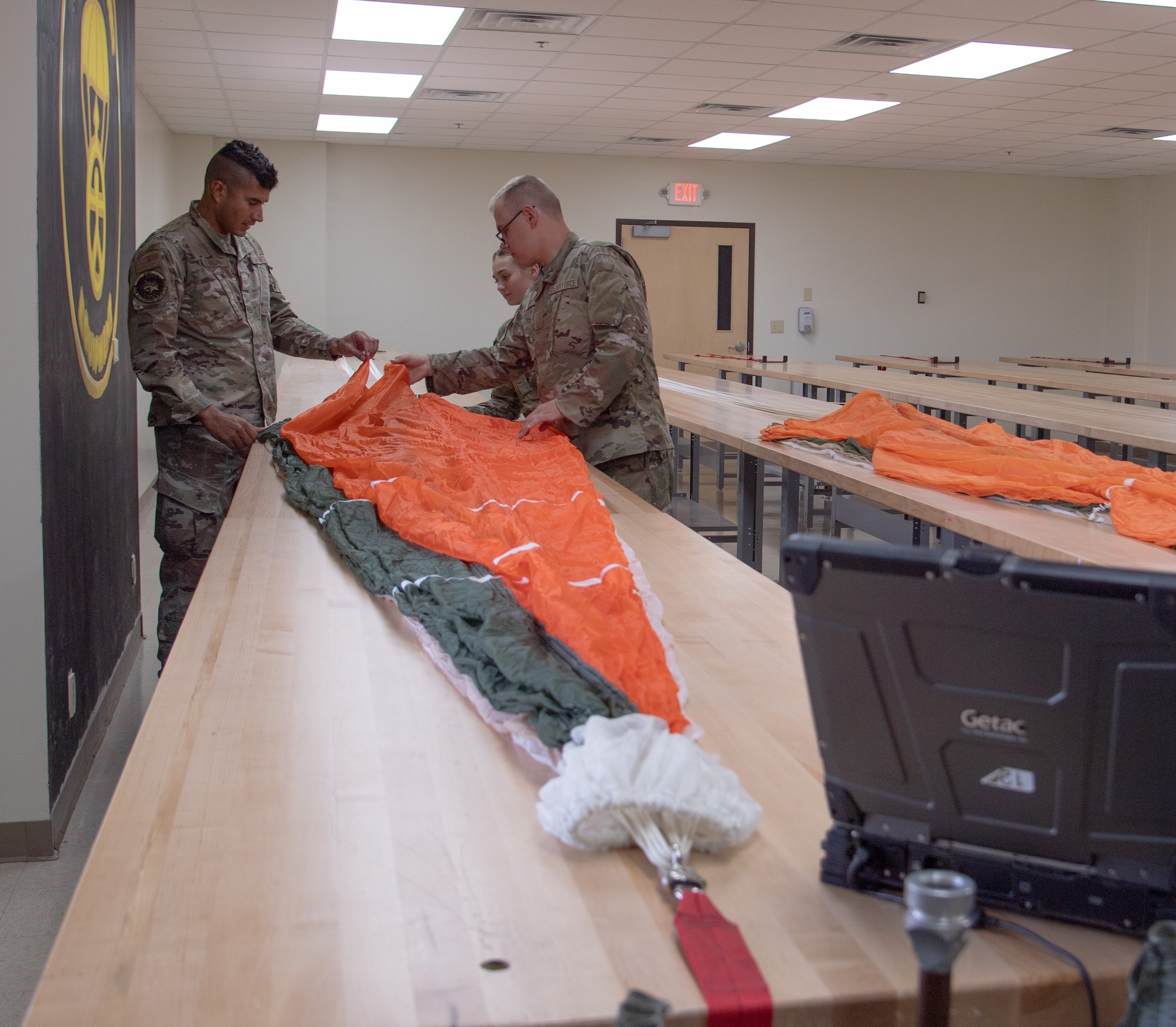 Two Airmen work on an orange and white parachute