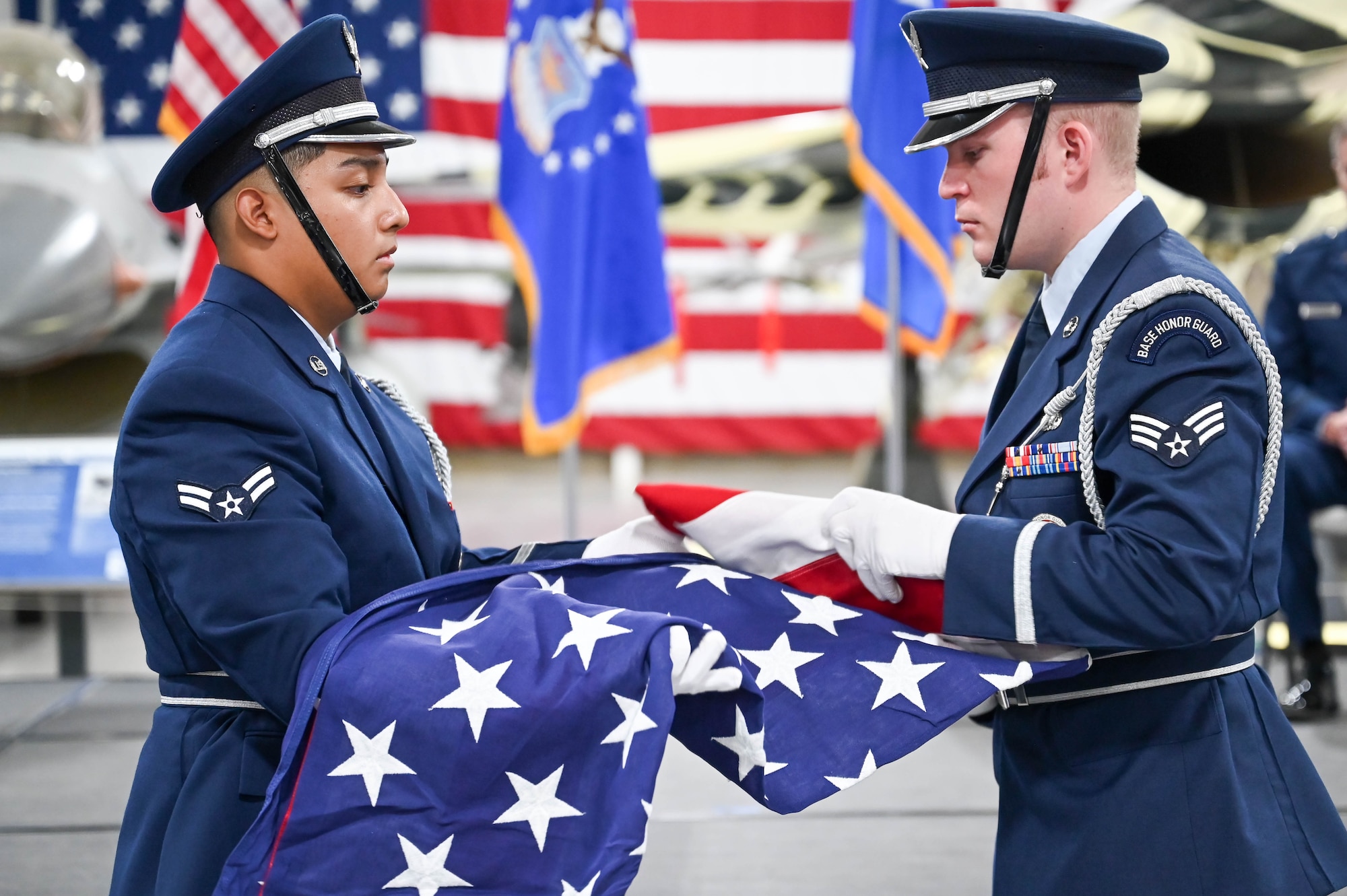 Two airmen in dress blues fold an American flag.