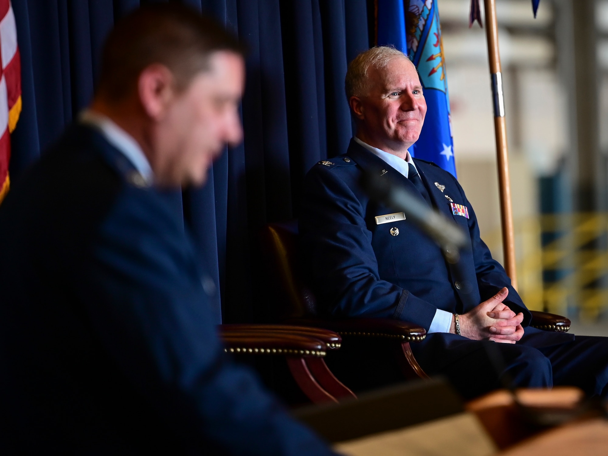 A man in Air Force blue dress uniform sits in a chair during a ceremony.