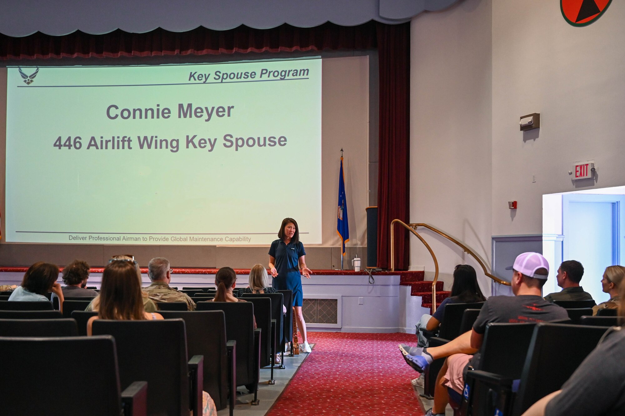 Audience members sit in theater style seating while a woman gives a presentation.