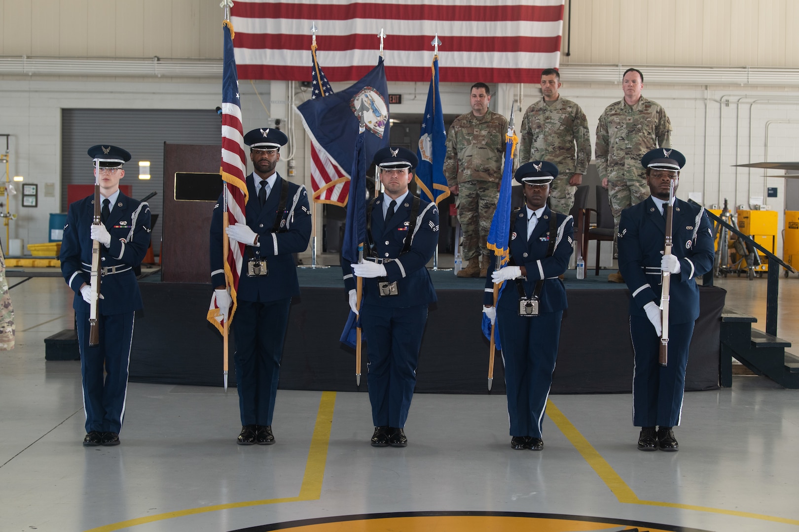 Colonels stand on stage and honor guard presents colors in front of stage.