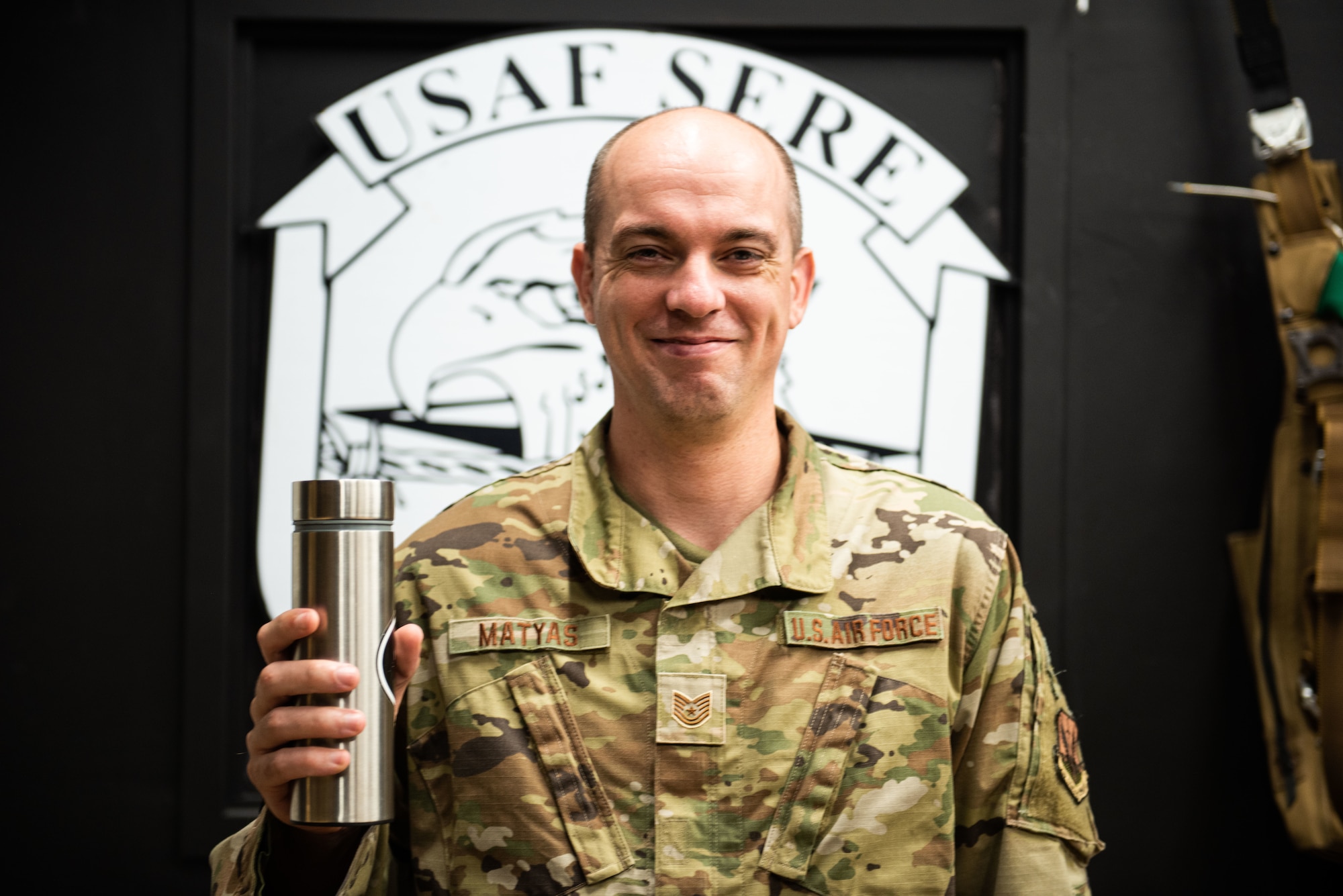 United States Airmen smiles at camera while he holds a cylinder-shaped titanium filtration water bottle.
