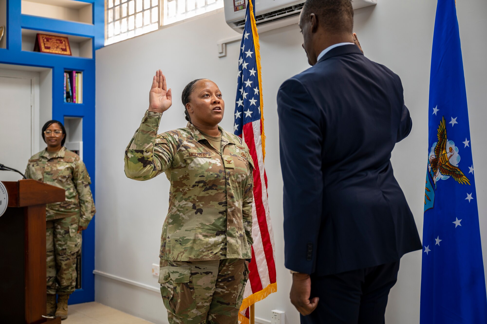 A military member in uniform stands holding her right hand up and repeating an oath.