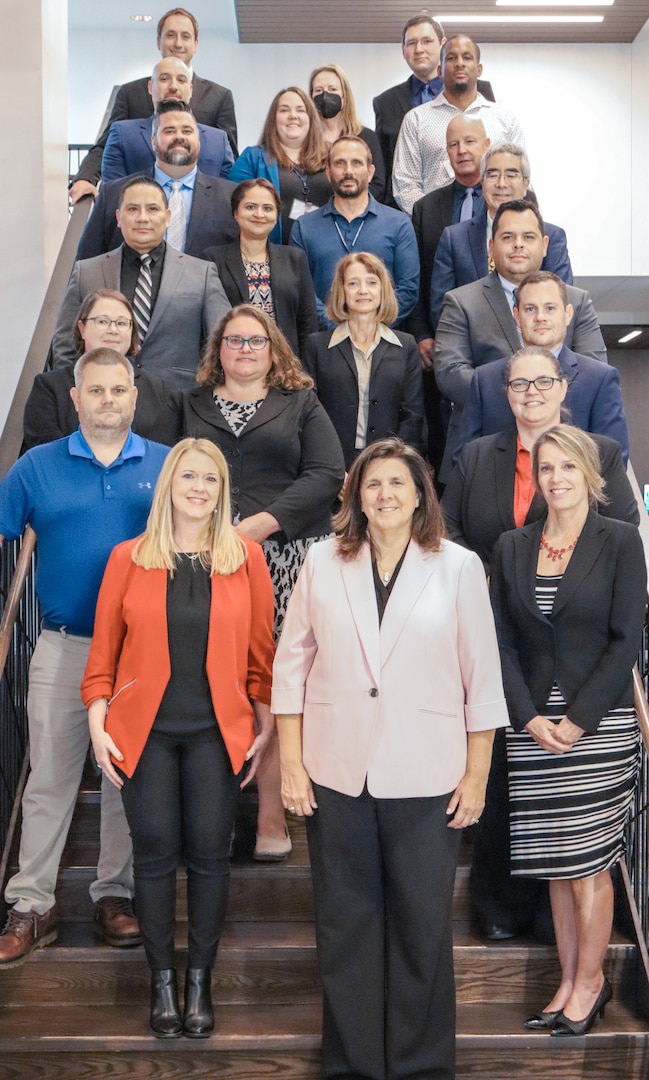 23 men and women dressed in business attire on a stairway posing for photos