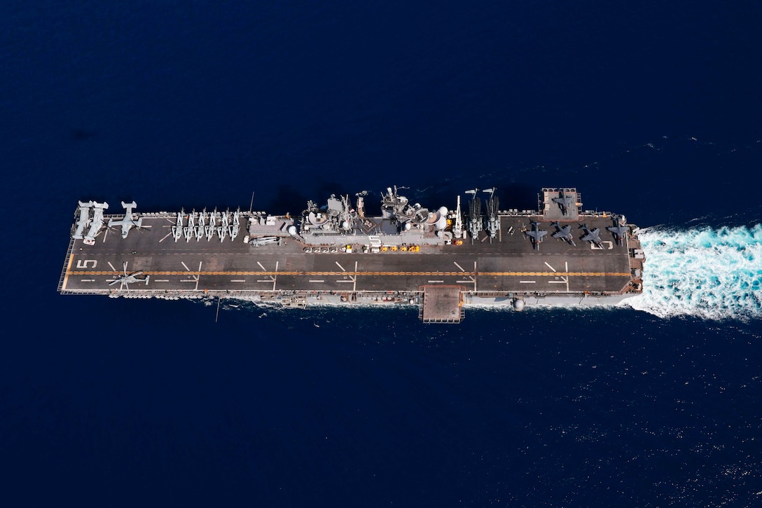 Aircraft are parked on the deck of a ship as the ship travels through a body of water.