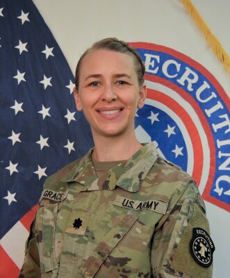 Woman wearing army uniform standing in front of US and USAREC flags