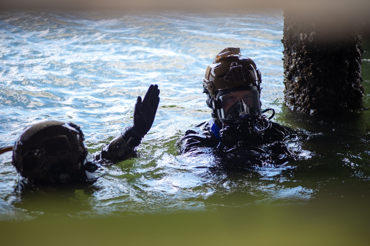 Two sailors in dive gear move through a body of water.