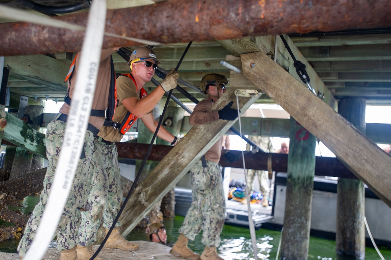A sailor attaches a bolt to a mount truss under a bridge.