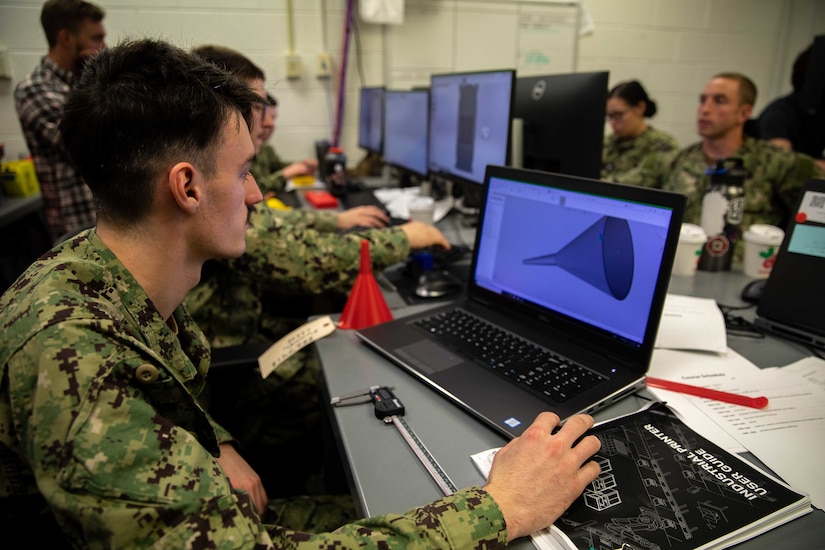 A man in uniform looks at a 3D model on a laptop computer.