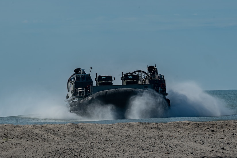 An air-cushioned landing craft lands on a beach.