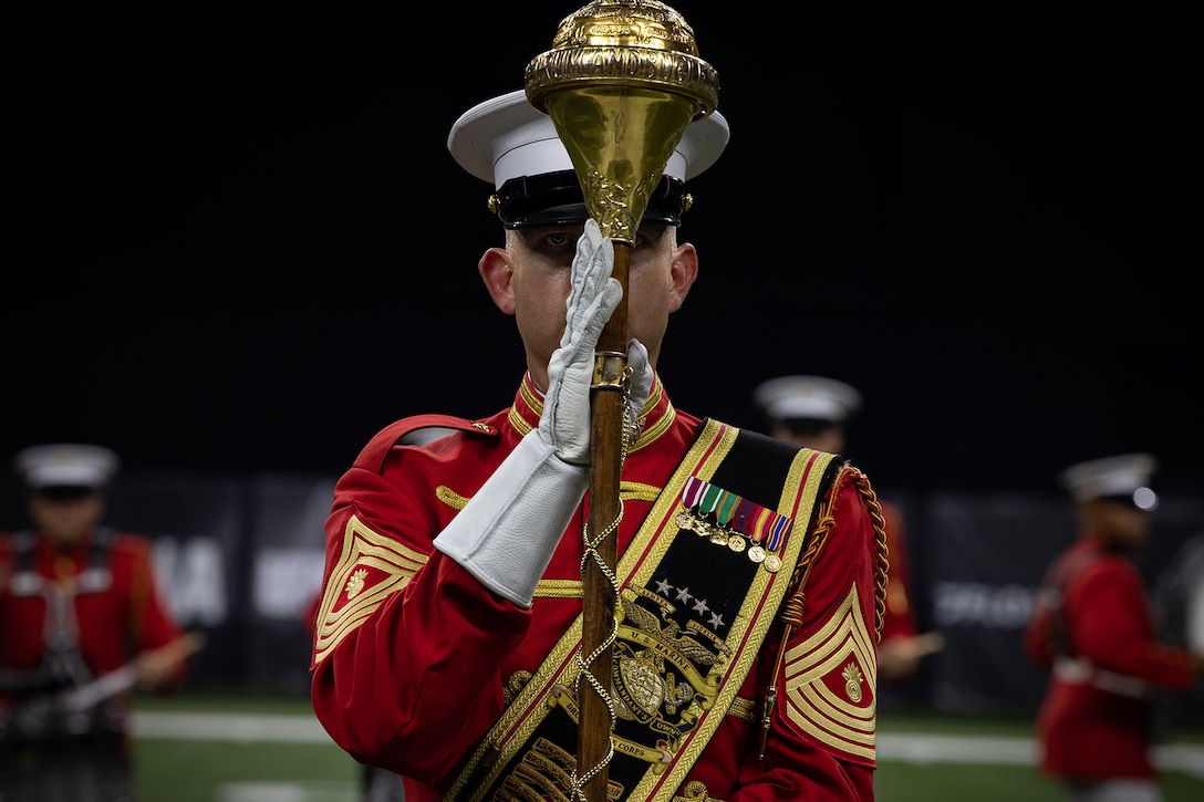 A Marine dressed in a ceremonial band uniform holds a staff.