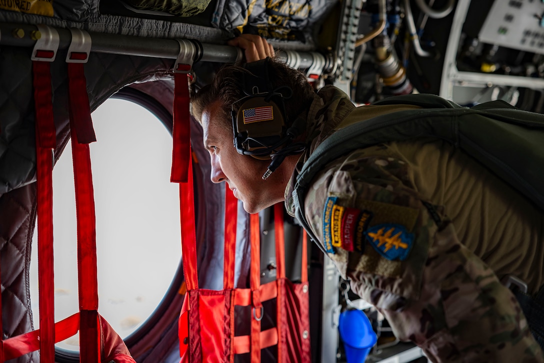 A service member looks out the window of an aircraft.