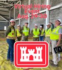 7 men wearing yellow work vests and hard hats inspect a building under construction.