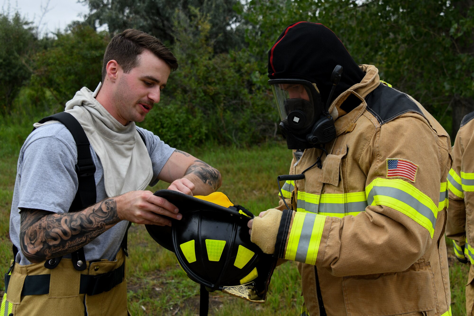 A man helps another man put on firefighter gear.
