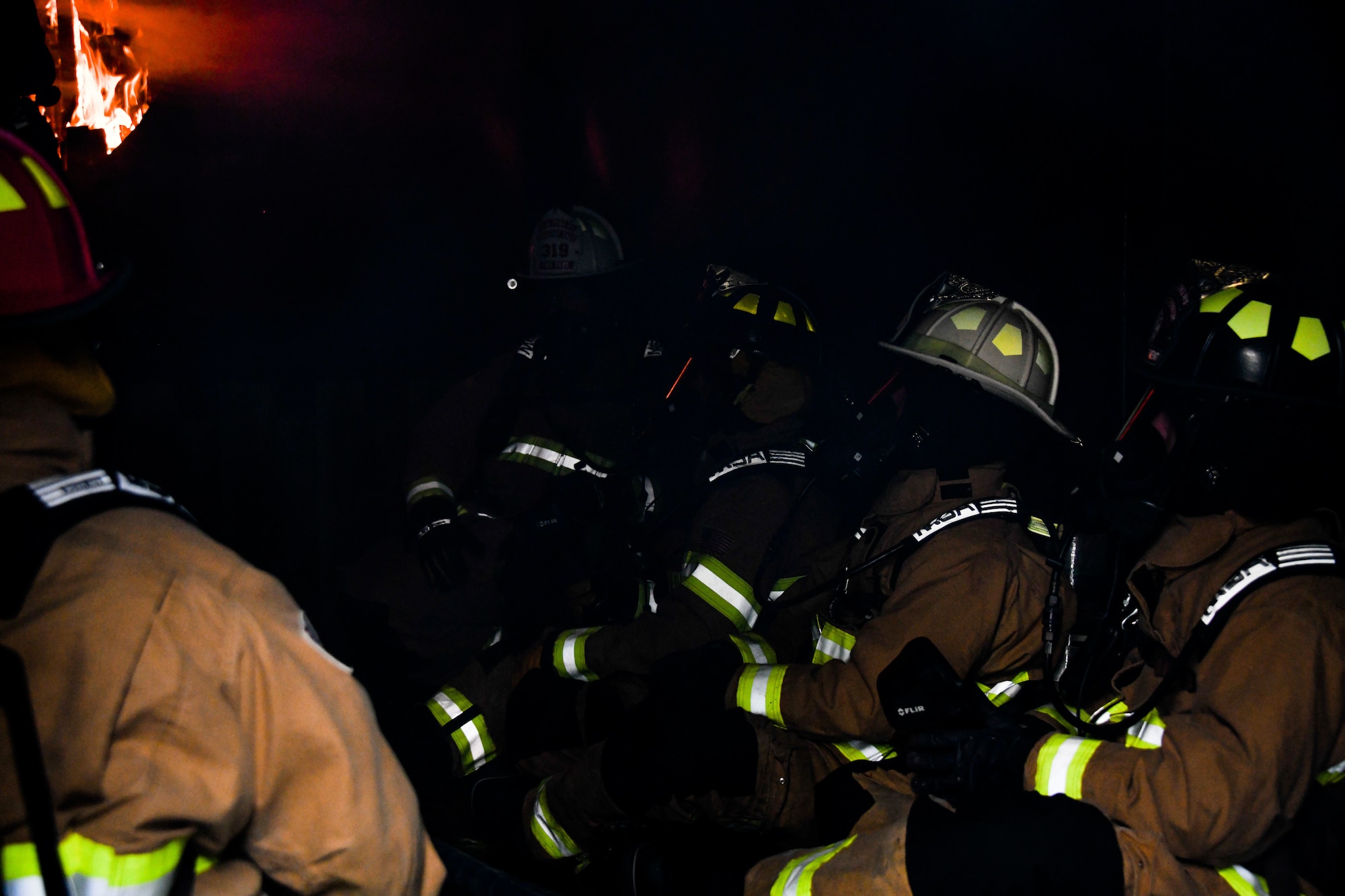 A group of firefighters stand together in a burning structure.
