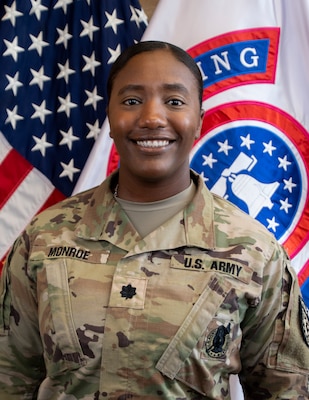 Female Soldier posed in front of the U.S. flag and the USREC flag.