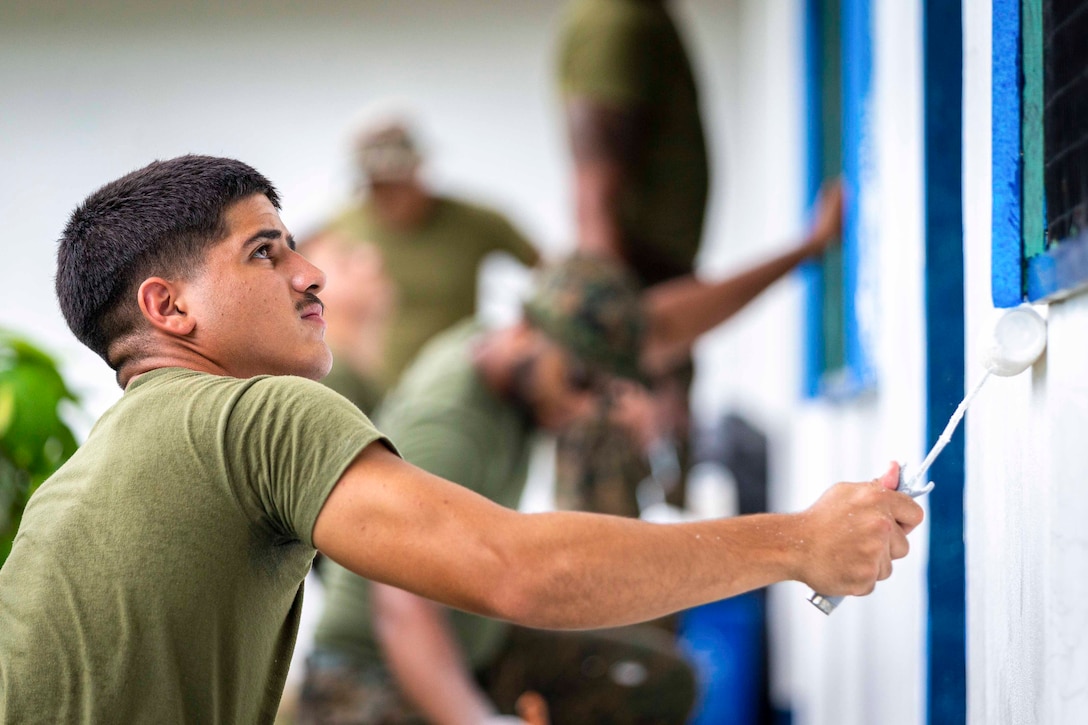 A Marine uses a paint roller to paint a wall.