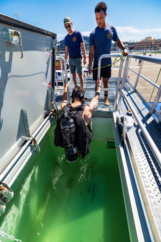 Navy Diver Petty Officer First Class Christian Stewart and Navy Diver Petty Officer Third Class Giovanni Alwadi help Navy Diver Petty Officer First Class, Jeremy Melson into the dive tank at Pier 46 in downtown Seattle, Aug. 3, 2023, in support of the Fleet Week portion of Seafair. (U.S Navy Photo by Wendy Hallmark)