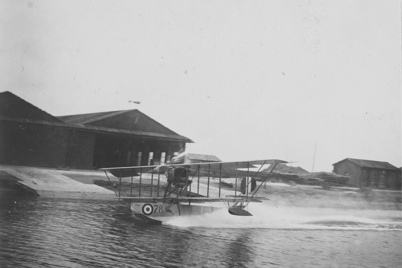 An airplane lands on water. A building sits in the background.