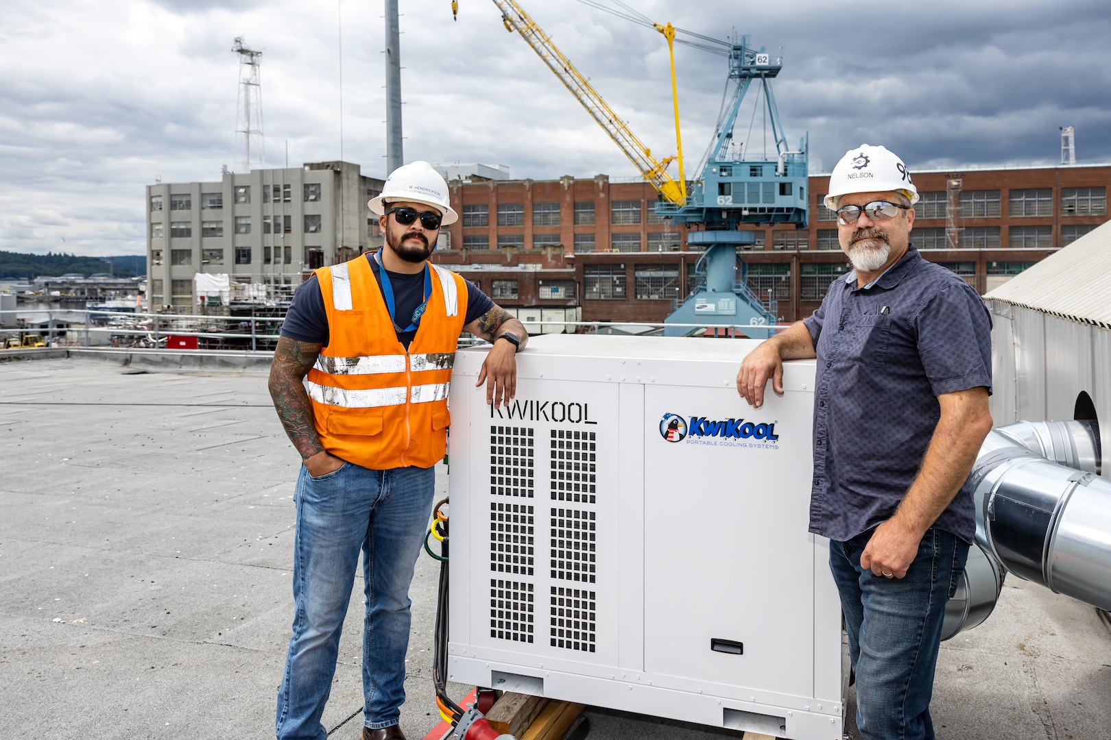 Matt Hendrickson and Brad Nelson pose alongside one of the newly installed temporary cooling systems on the roof of Building 879 at Puget Sound Naval Shipyard & Intermediate Maintenance Facility in Bremerton, Washington. (U.S. Navy photo by Jeb Fach)