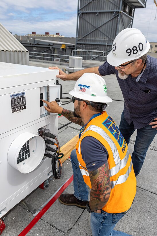 Brad Nelson, right, project manager, Code 980X, Project Management, and Matt Hendrickson, utilities general foreman, Workcenter 57, Electrical Construction Team, examine one of the recently installed temporary cooling systems on the roof of Building 879 at Puget Sound Naval Shipyard & Intermediate Maintenance Facility in Bremerton, Washington. (U.S. Navy photo by Jeb Fach)