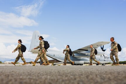Uniformed service members walk across a tarmac with a military aircraft behind them.