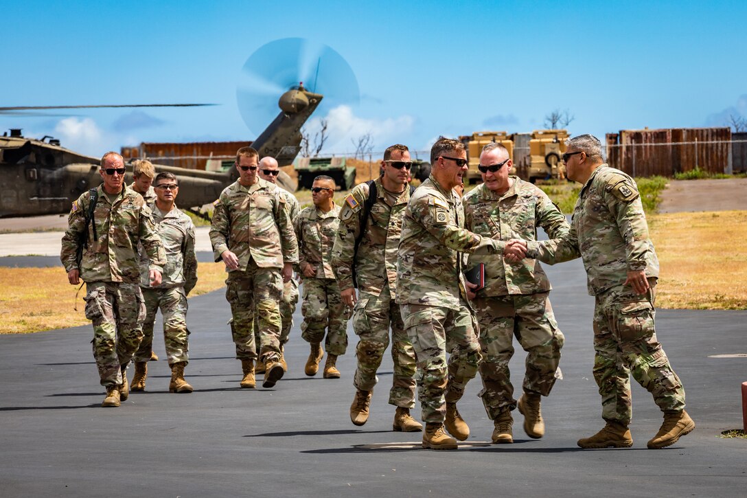 A group of soldiers walk on a tarmac with two in the front shaking hands.