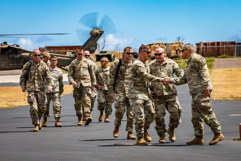 A group of soldiers walk on a tarmac with two in the front shaking hands.