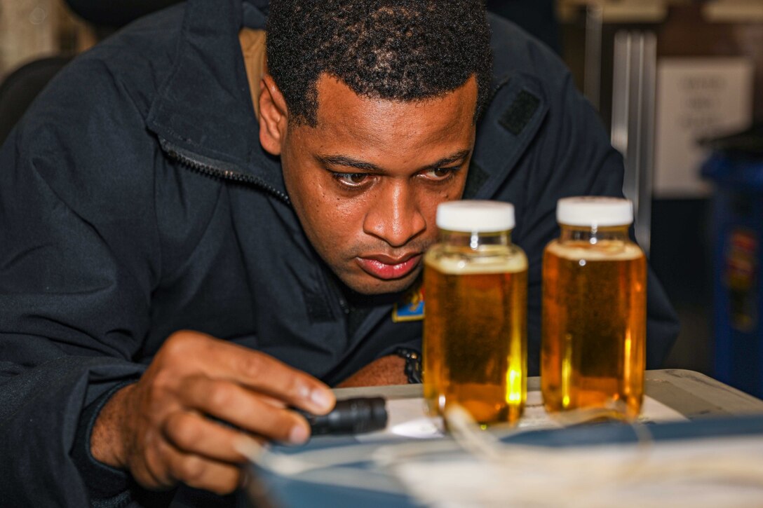 A sailor looks closely as two bottle of oil.