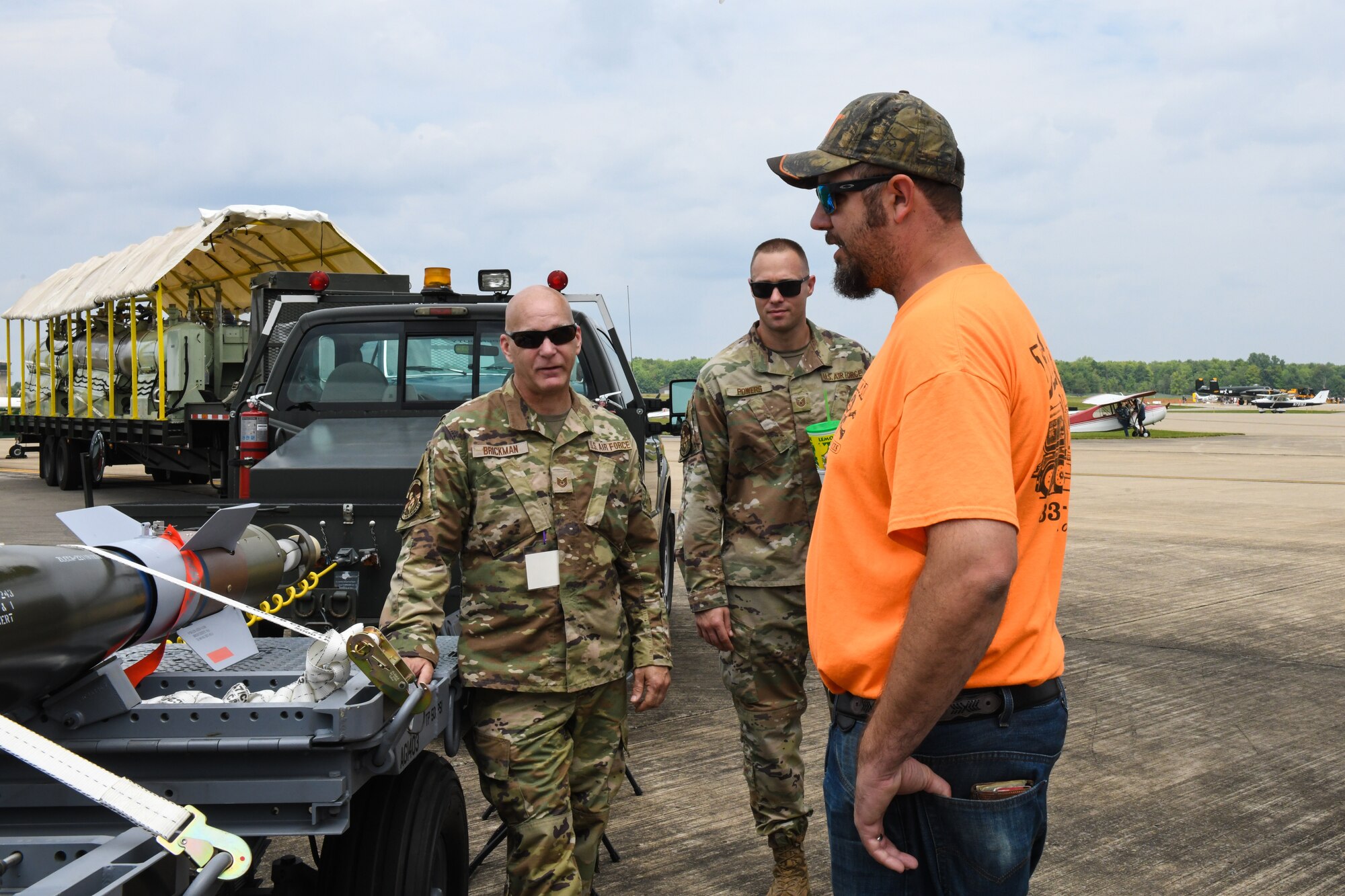 Tech. Sgt. John Brickman (left), a munition storage technician, and Tech. Sgt. Hunter Powers (middle) NCOIC of munitions operations, both assigned to the 910th Maintenance Squadron, talks with event guests, Aug. 6, 2023, at the Wings and Wheels Fly-In and Car Show at Youngstown-Warren Regional Airport, Ohio.