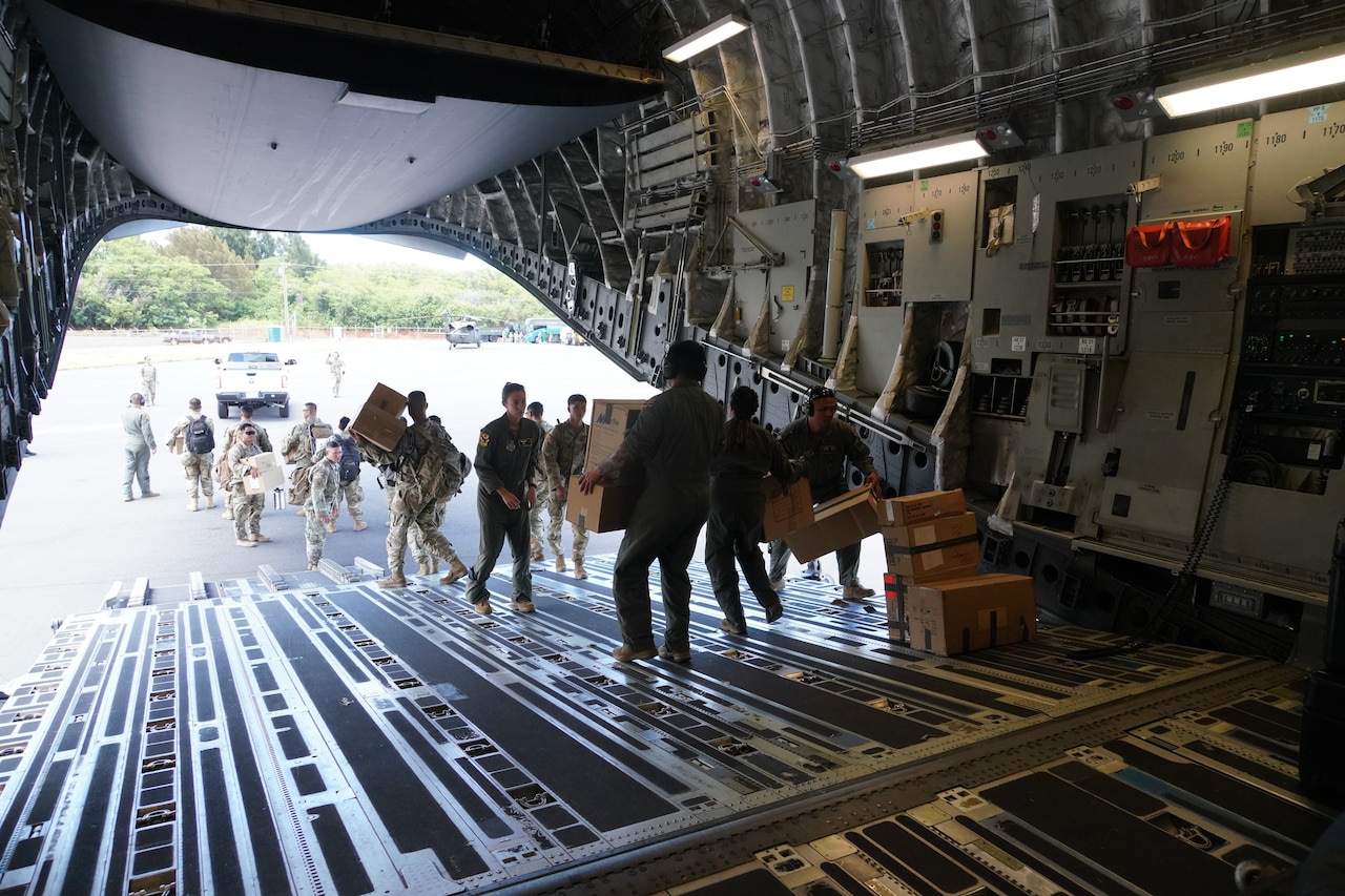 Uniformed service members unload boxes from a military aircraft.