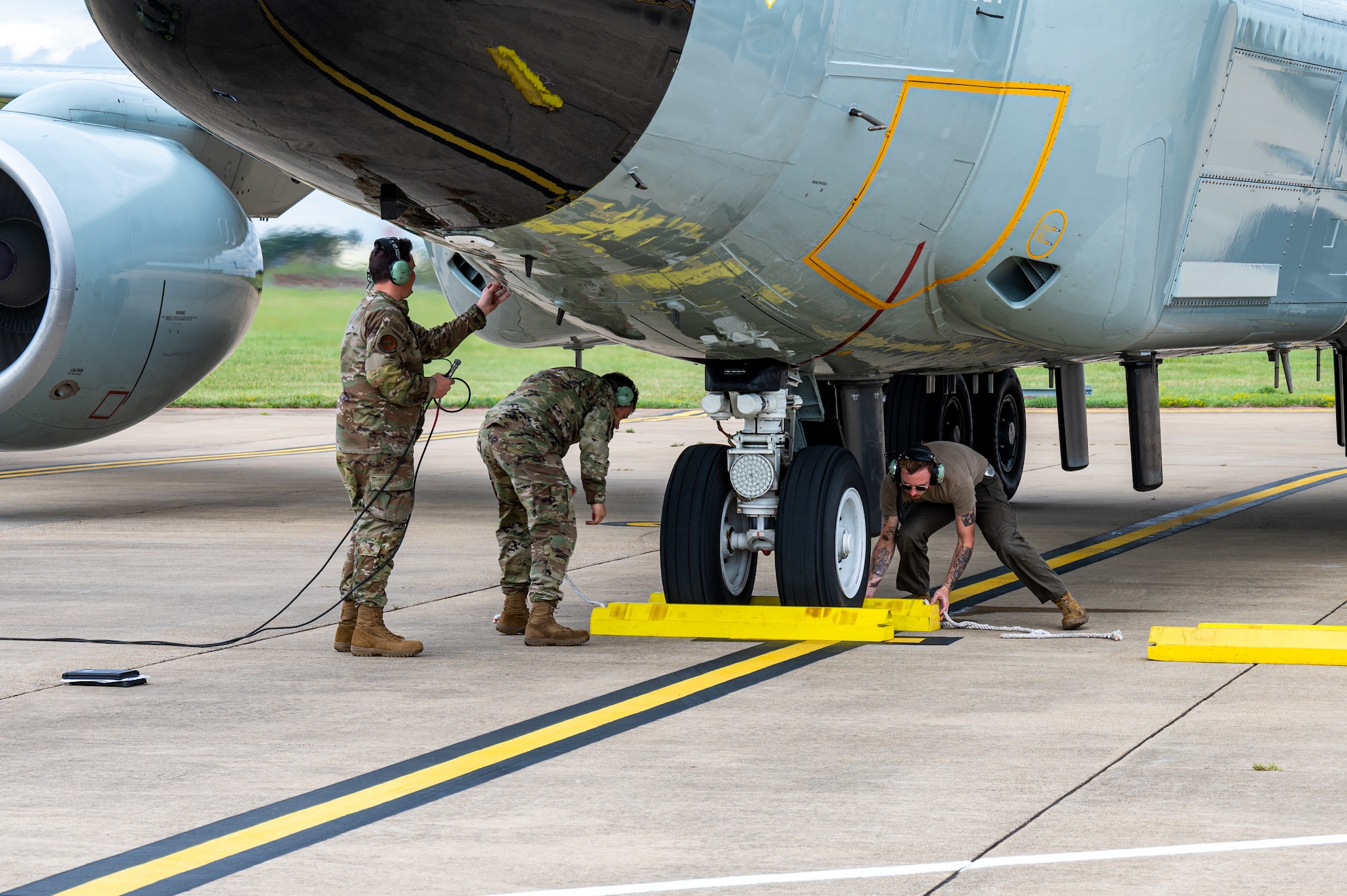 U.S. Air Force maintenance Airmen, assigned to the 95th Reconnaissance Squadron, place wheel chocks around the nose gear of a RC-135 Rivet Joint aircraft to begin the first hot-pit refueling mission for the airframe at Royal Air Force Mildenhall, England, Aug. 14, 2023.