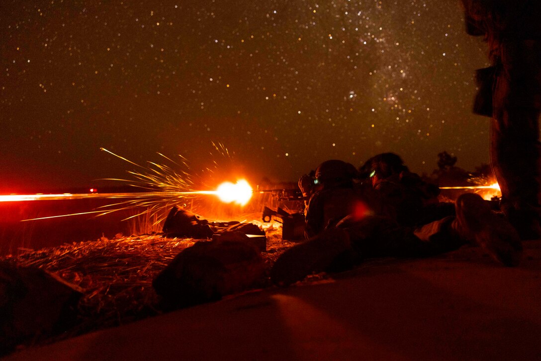 The red glow from weapons being fired by Marines shows under a starry sky.