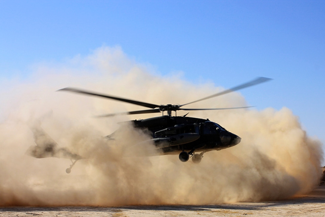 A helicopter hovers over the ground as dust swirls around it.