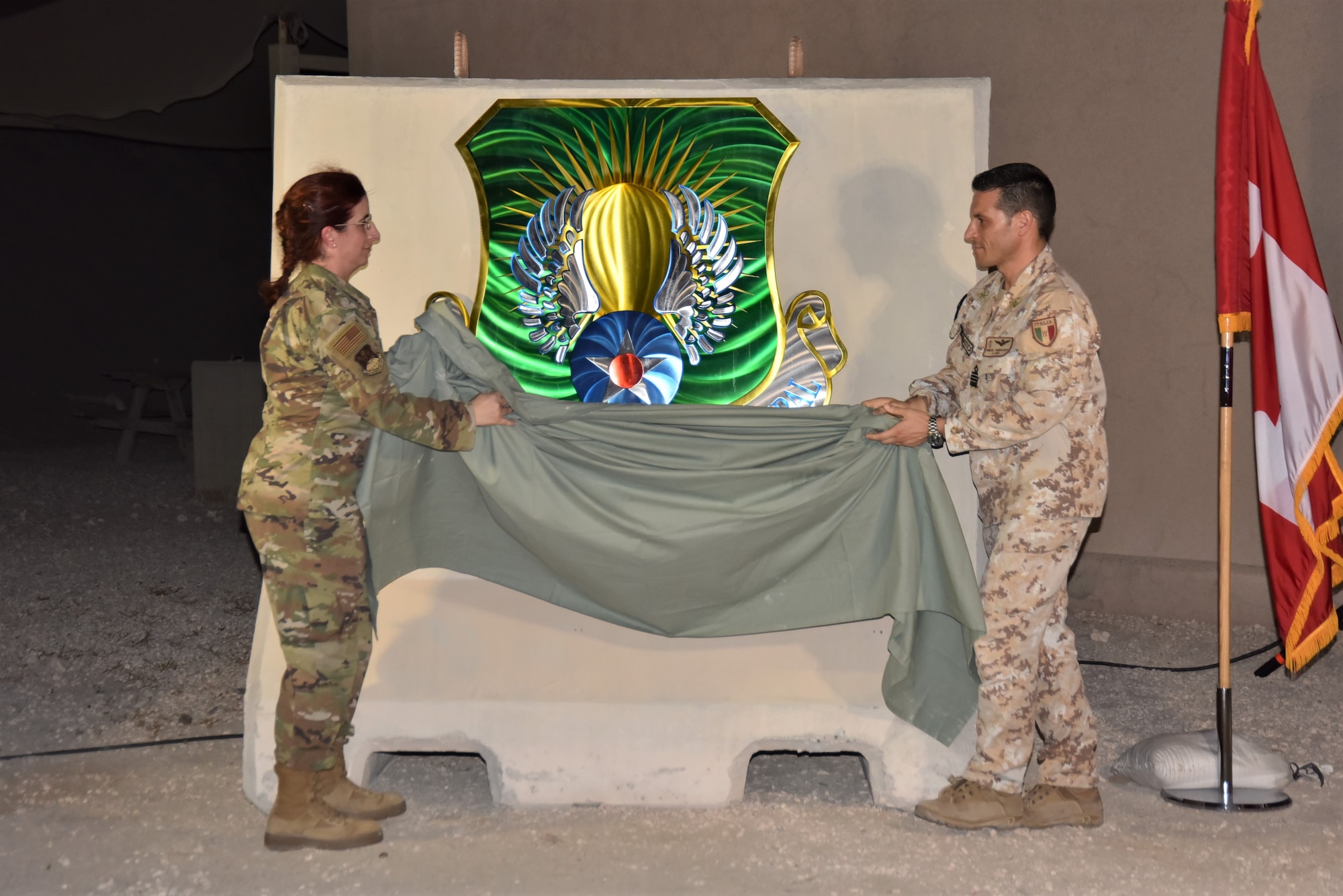 U.S. Air Force Col. Julie Sposito-Salceies, 609th Air Operations Center commander, left, and Italian Air Force Col. Emilio Fanigliulo, lead senior national representative, unveil the new coalition and combined forces central emblem August 16, 2023, at Al Udeid Air Base, Qatar.