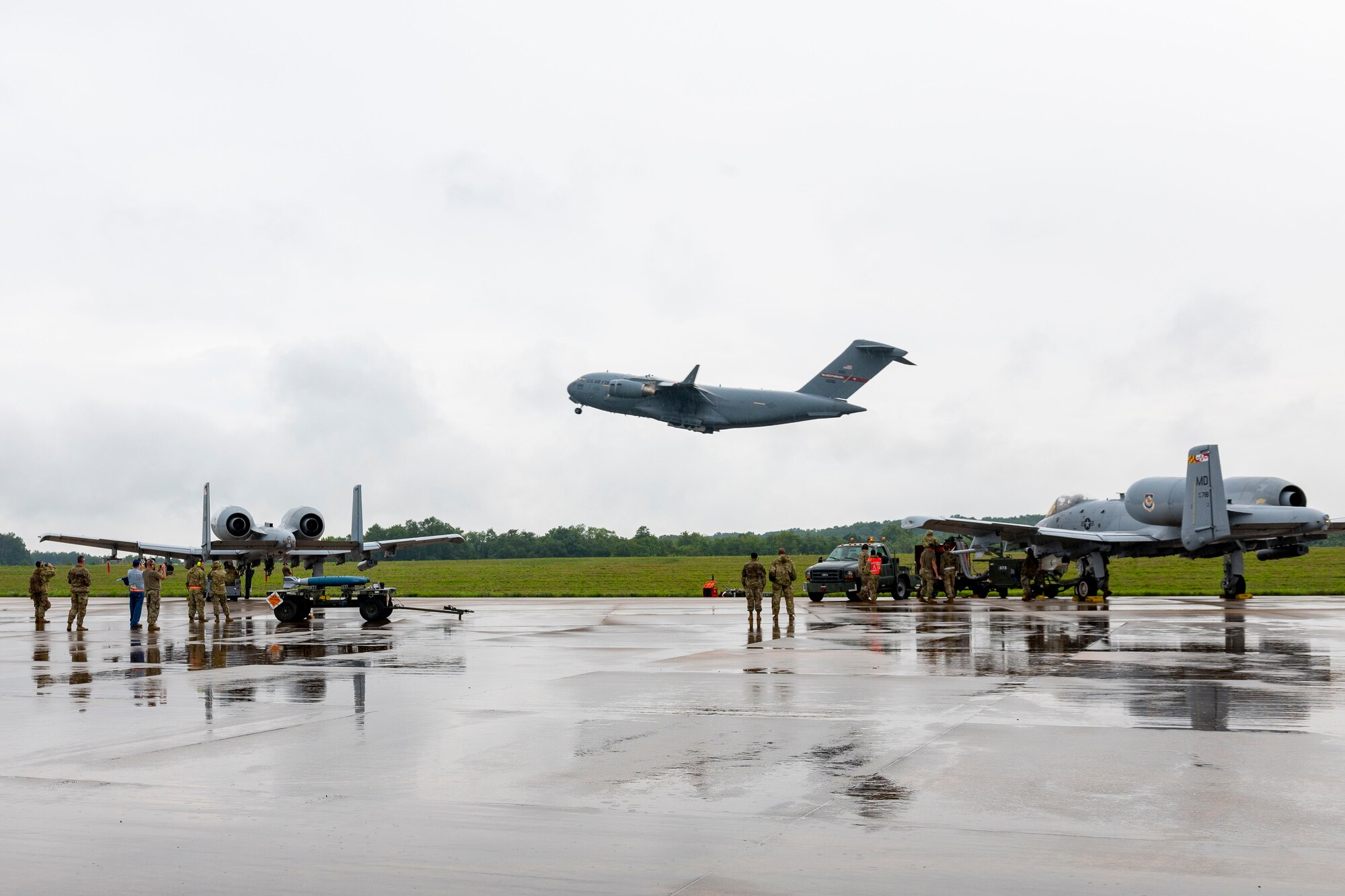 A C-17 Globemaster III aircraft launches for a training sortie while munitions are loaded to two A-10 Thunderbolt II aircraft at Shepherd Field, Martinsburg, West Virginia, Aug. 10, 2023.