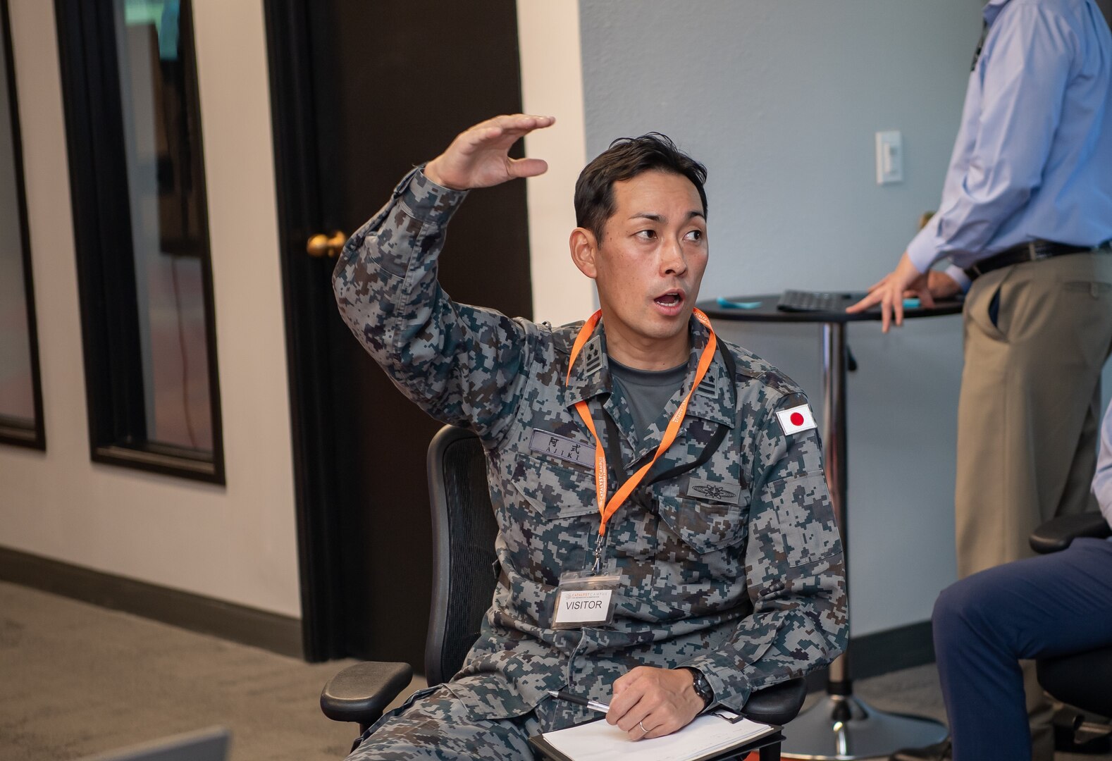 Man in Japanese military uniform speaks with his hand up in the air