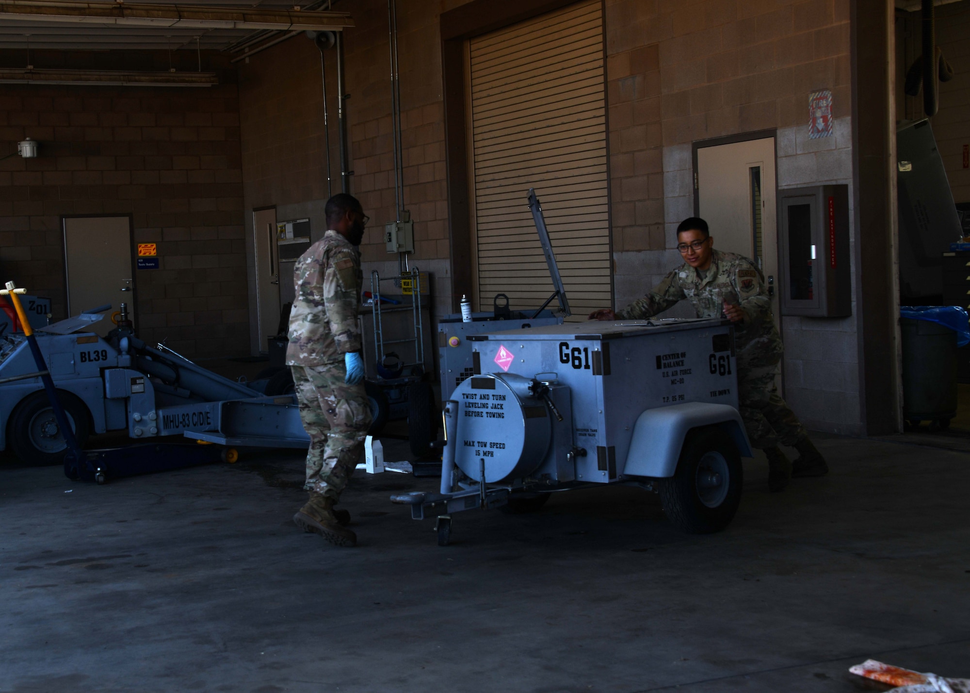A US service member wearing green camo pushes a metal cart from the right of the frame to the left