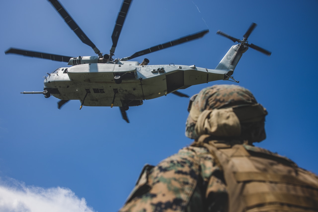 A Marine looks up at an airborne helicopter.